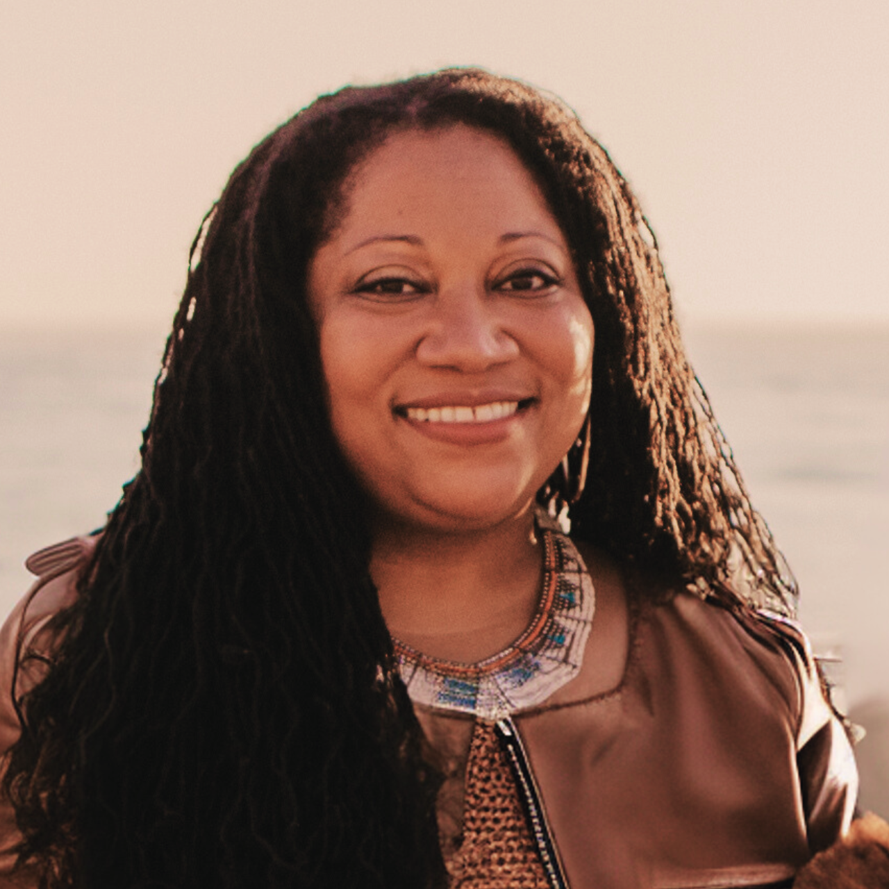 Headshot of Dr. Jamila Moore Pewu in brown leather jacket with blurred background