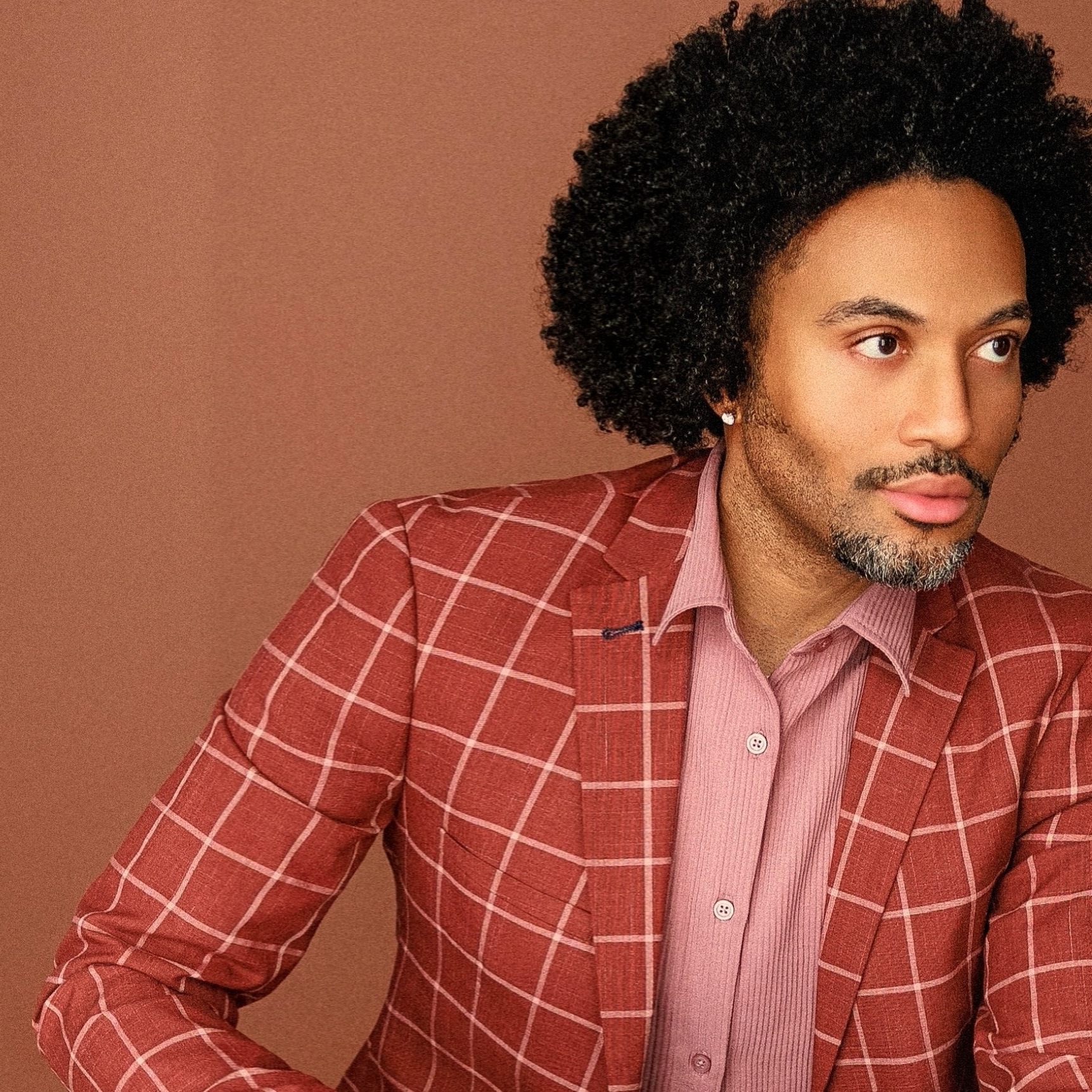 A professional headshot of Dr. La Marr Jurell Bruce, with an afro hairstyle and sporting a striking redish plaid suit.