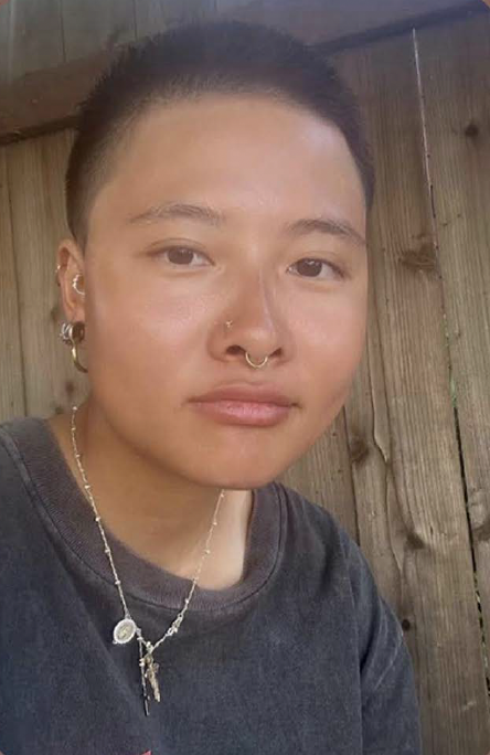 Headshot of Milla Wu with short dark hair, wearing a Black shirt. Images is set against a wood toned background. 